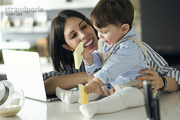 Baby boy and mother playing with adhesive notes at home