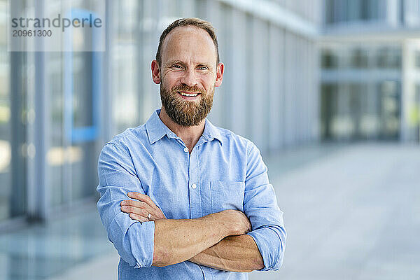 Casual businessman standing in front of office building with arms crossed