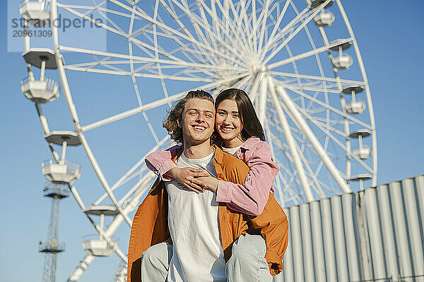 Smiling couple standing in front of ferris wheel at amusement park