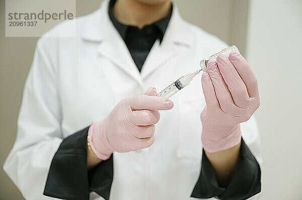 Aesthetician wearing glove and filling syringe through vial at clinic