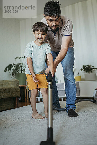 Father and son cleaning carpet with vacuum cleaner at home