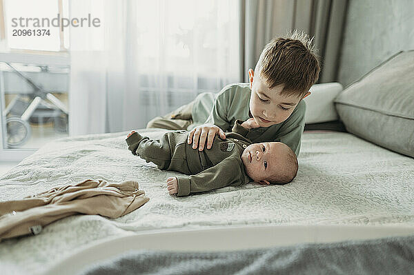 Cute boy watching over baby brother lying on bed at home