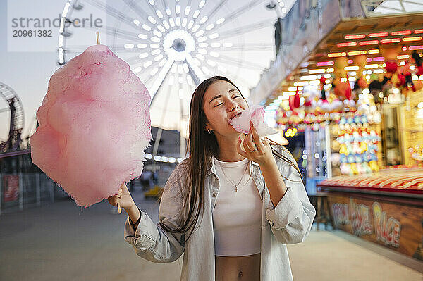 Smiling girl with eyes closed eating cotton candy at amusement park