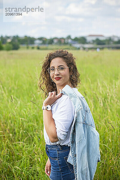 Young woman holding denim jacket and standing at field