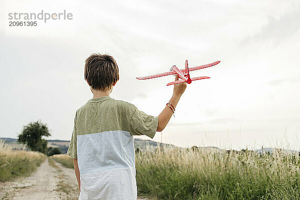 Boy playing with red airplane on field