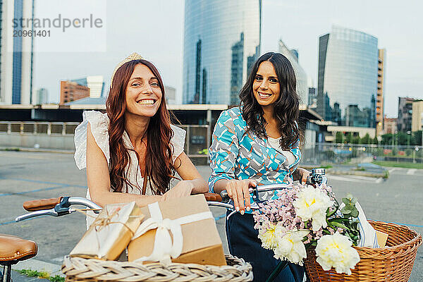 Happy friends standing with bicycles and gifts in front of buildings