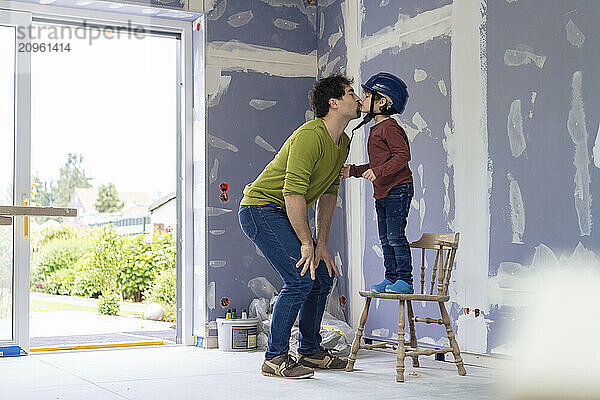 Father kissing son standing on chair in new apartment