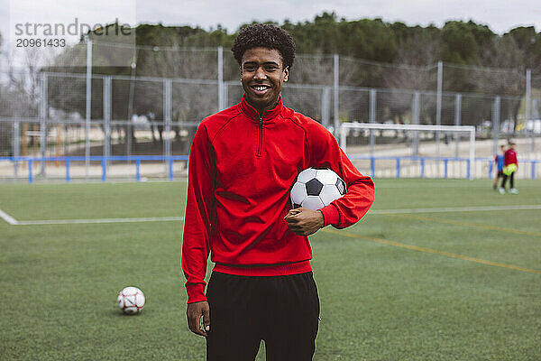 Smiling soccer player standing with ball on field