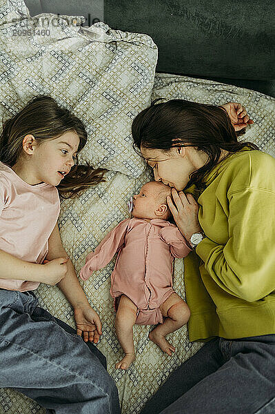 Mother kissing baby and lying down with daughter on bed