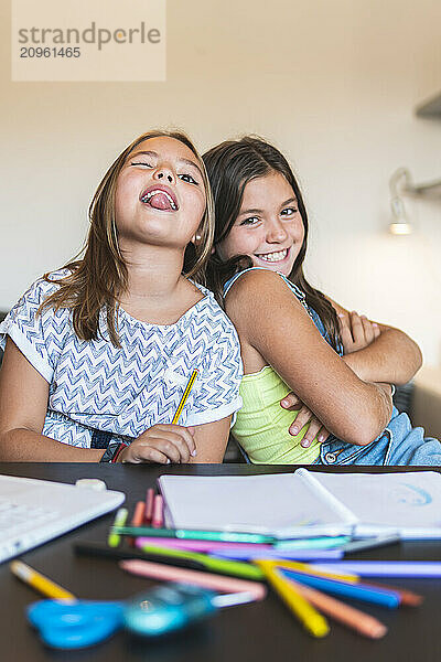 Girl leaning on friend sticking out tongue at home