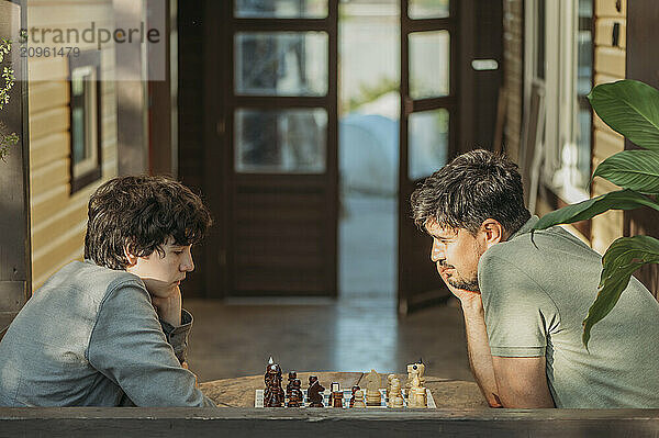 Father and son playing chess sitting at table on porch