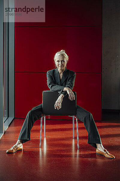 Businesswoman sitting with legs apart on chair near red wall