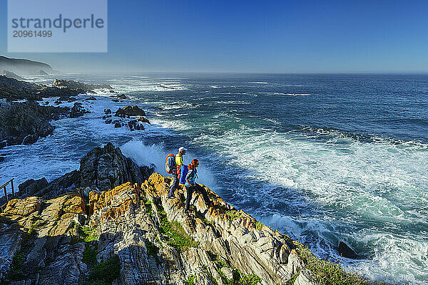 Hikers standing on rock and looking at wavy sea in Eastern Cape  South Africa