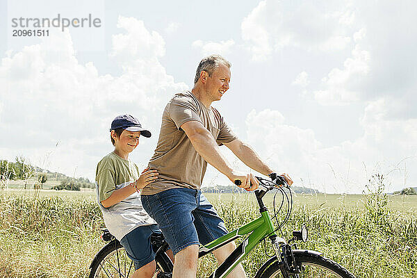 Son sitting behind father riding bicycle near field