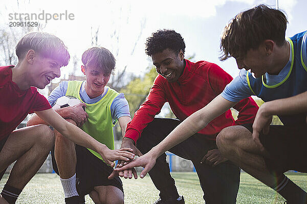 Happy soccer team stacking hands together on field