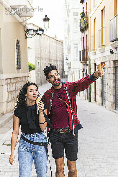 Man holding ice cream and pointing next to girlfriend walking at street