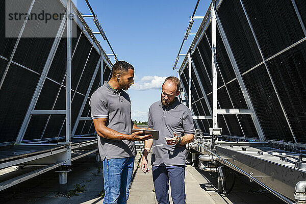 Two employees with digital tablet talking on rooftop beside refrigeration installation