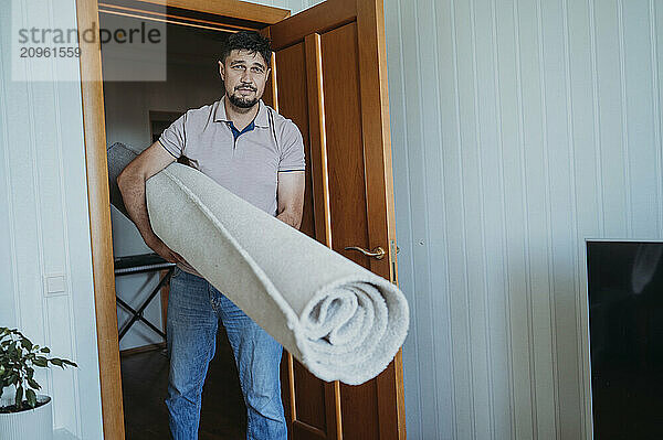 Mature man carrying carpet and standing at home