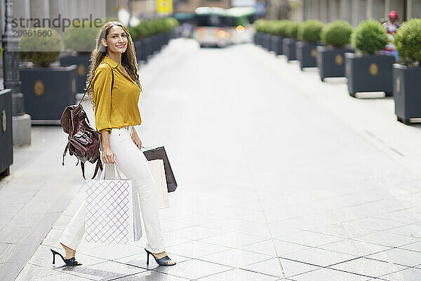 Woman with backpack holding shopping bags and crossing road in city