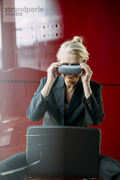 Smiling businesswoman holding virtual reality headset sitting on chair