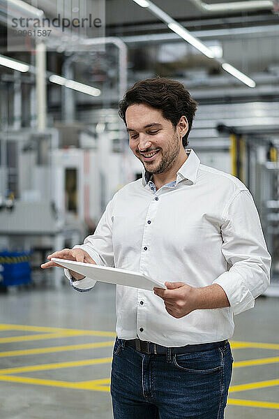 Smiling young businessman using tablet PC at factory