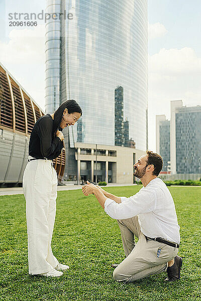 Happy man proposing woman in front of buildings