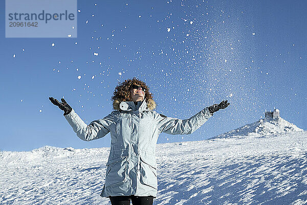 Carefree woman in warm clothing enjoying snow at mountain during winter