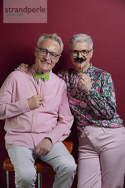 Happy senior couple posing with fake moustache and bowtie