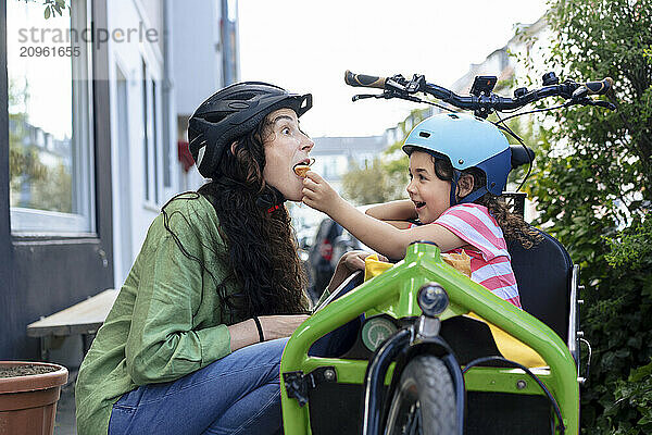 Girl sitting in cargo bike and feeding mother at street