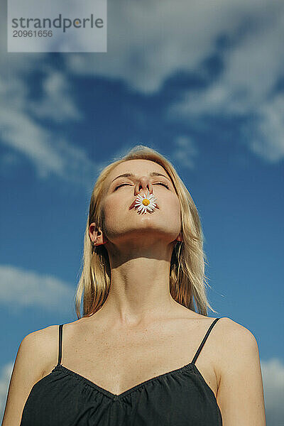 Beautiful woman with eyes closed holding daisy flower in mouth