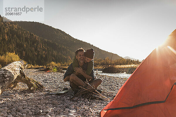 Mature woman embracing boyfriend sitting at riverside