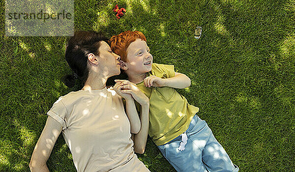 Mother kissing and lying next to son on grass in garden