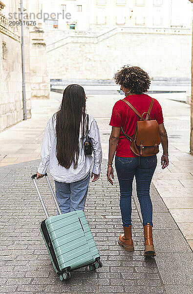 Friends with suitcase and backpack walking on street in city