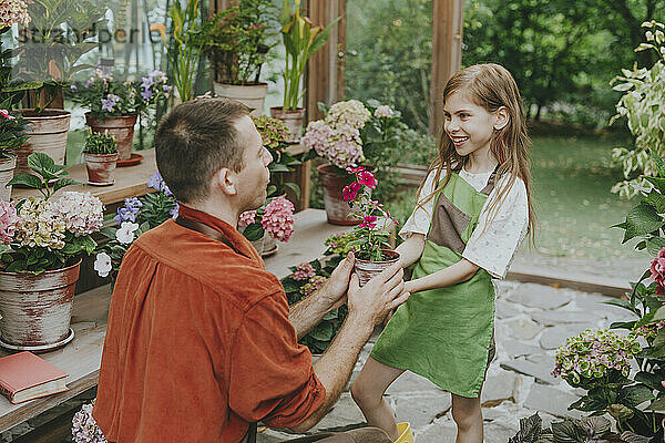 Father giving flower pot to daughter in greenhouse