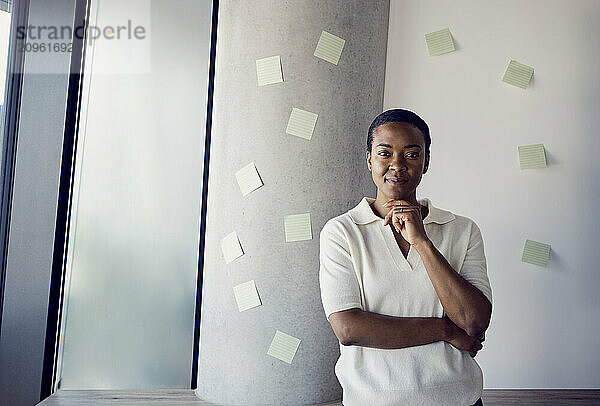 Confident businesswoman with hand on chin standing at office