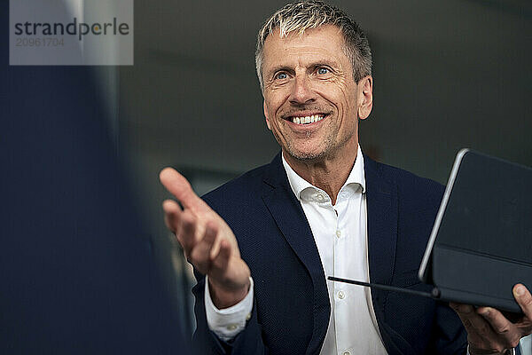 Smiling senior businessman holding tablet PC at office