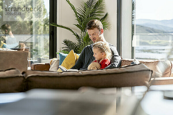 Smiling man reading book with daughter at home