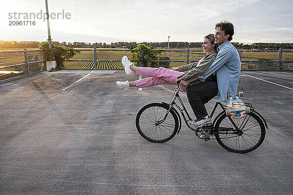 Boyfriend riding bicycle with girlfriend sitting on handlebar at parking lot