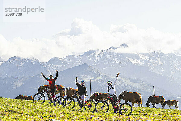 Friends waving hands and standing with bicycle amidst horses on mountain