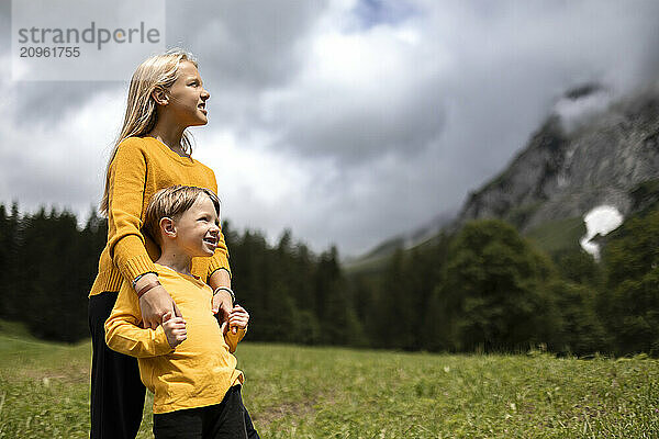 Brother and sister looking at view standing in meadow