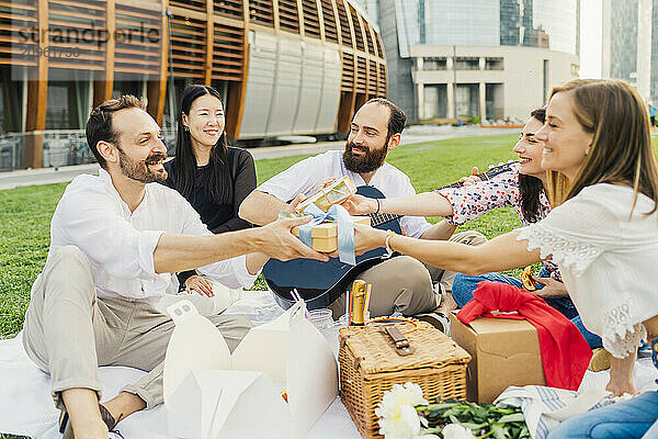 Happy women giving gifts to man and enjoying picnic in park