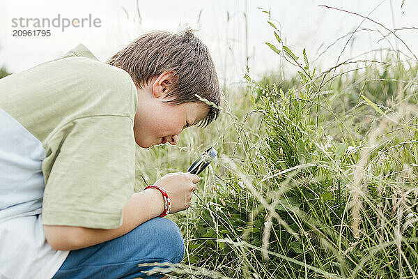 Boy crouching and examining grass through magnifying glass in field