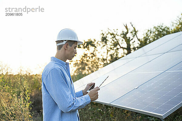 Engineer using tablet PC for examining solar panel in field