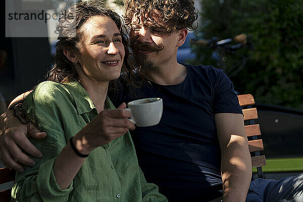 Man with arm around woman holding coffee cup at street