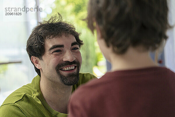 Happy father with goatee talking to son at home