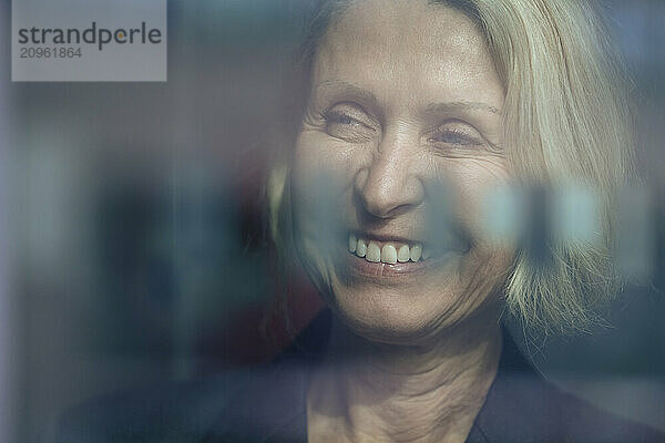 Happy senior businesswoman behind glass