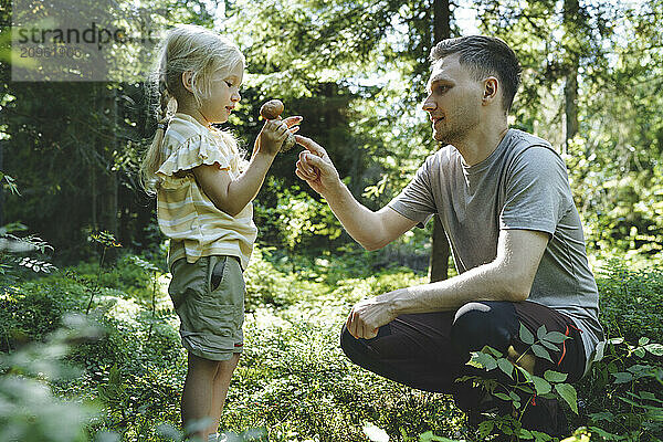 Father explaining about mushroom to daughter standing in forest