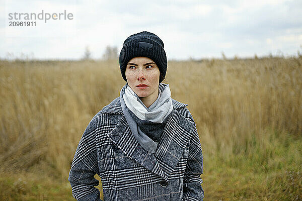 Thoughtful woman in warm clothes at field