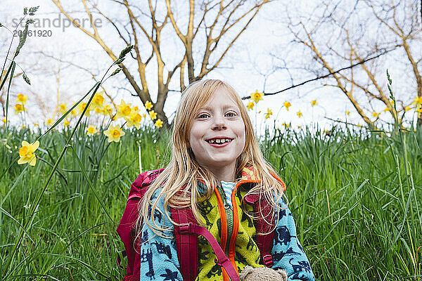 Smiling blond hair girl with backpack in daffodil field