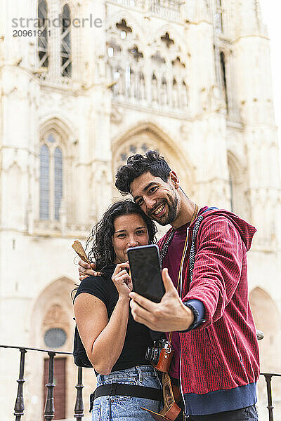 Smiling couple taking selfie through smart phone in front of Burgos Cathedral